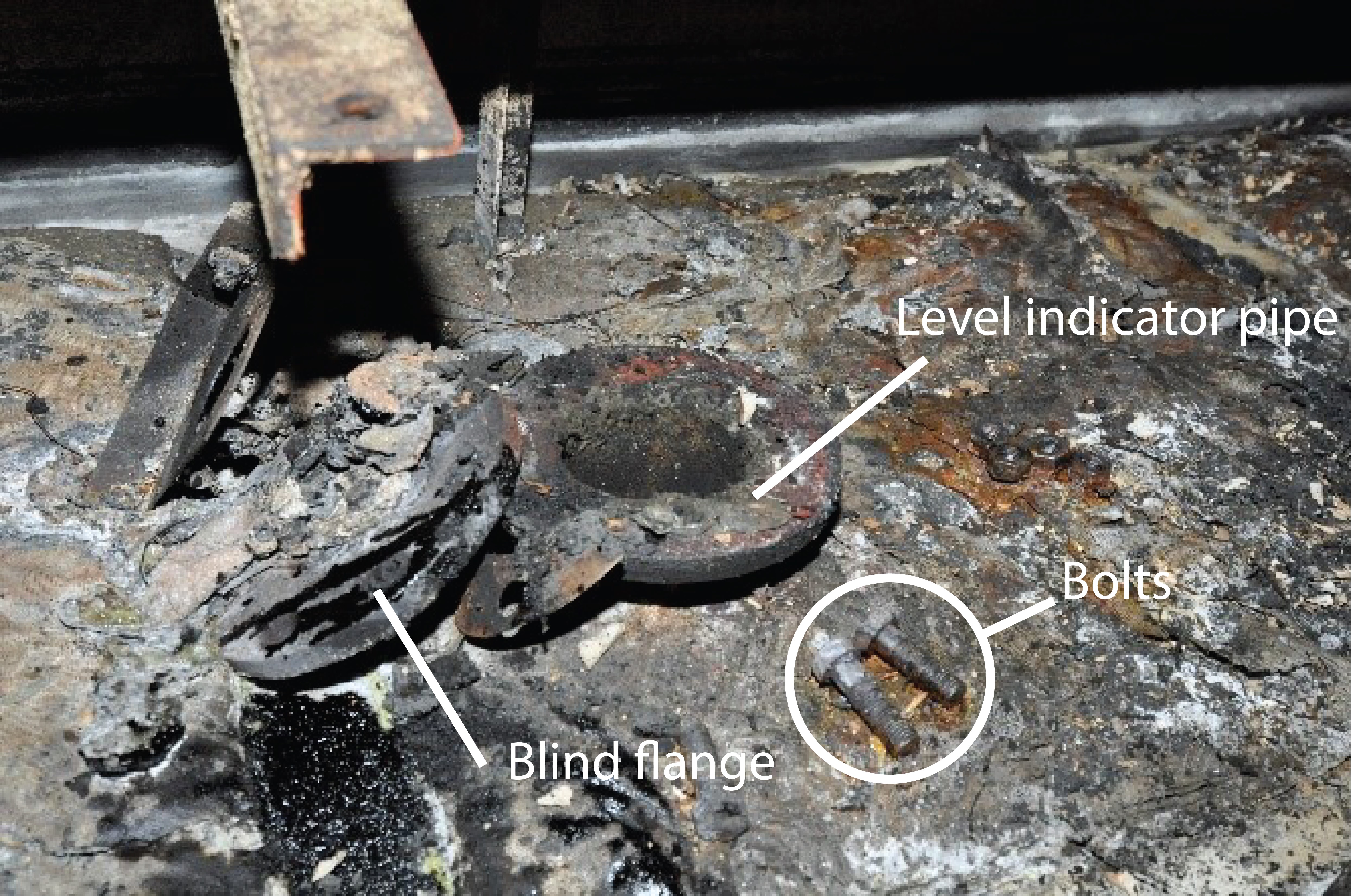 Opening of the level indicator pipe on top of the settling tank as found post-fire. Also shown are the blind flange, nuts, and bolts on top of the tank. (Source: TSB)